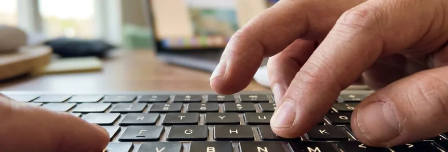 Gros plan sur des doigts tapant une adresse web sur le clavier rétroéclairé d'un ordinateur portable, avec un écran flouté en arrière-plan